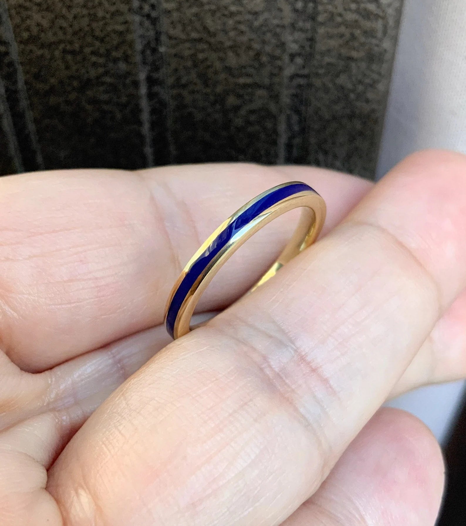 A close-up of a gold band ring with a dark blue inlay, held on a person's finger.