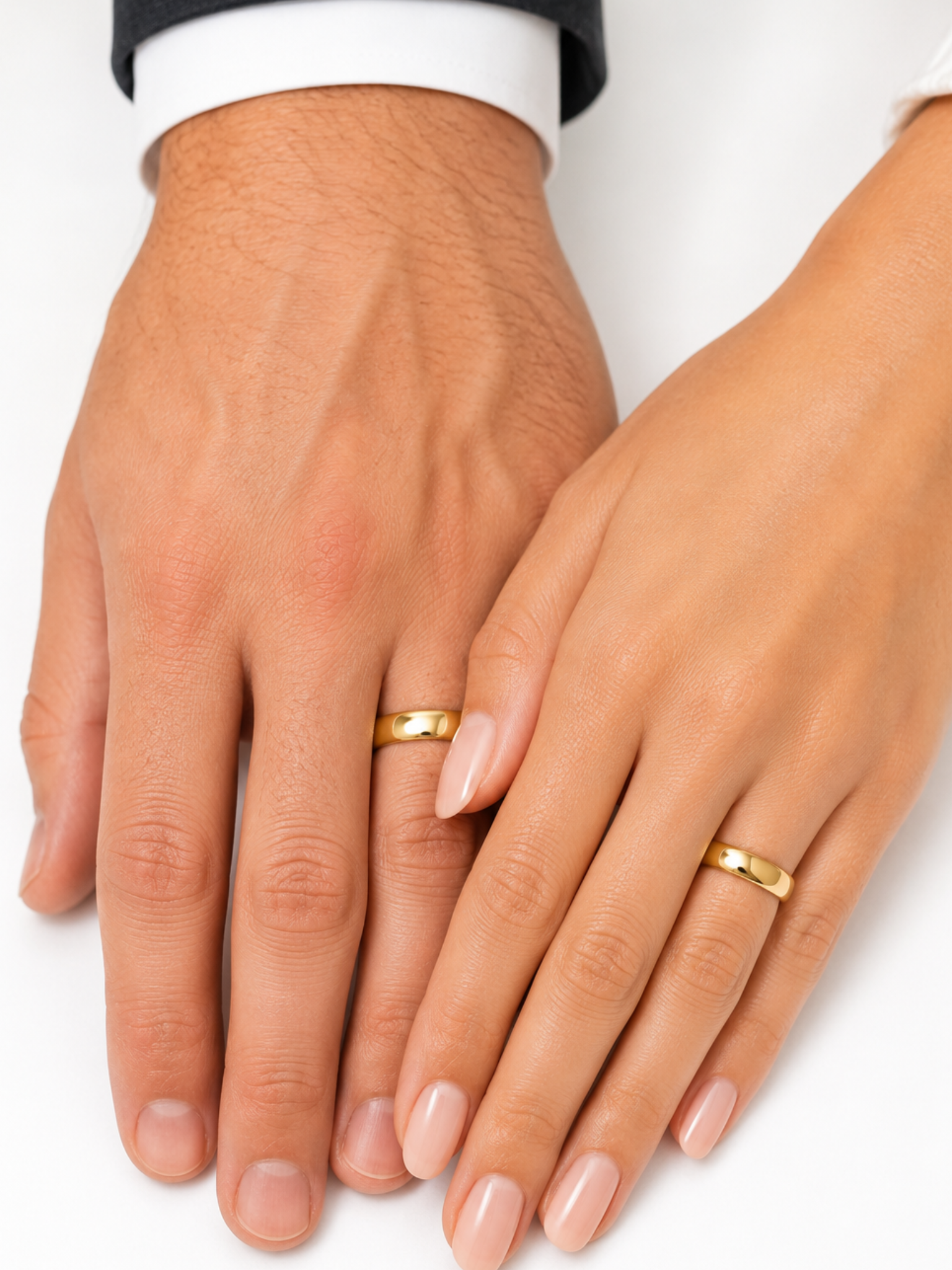 Man and woman's hands resting against each other, each wearing a 4mm wedding  band ring, plain white background.