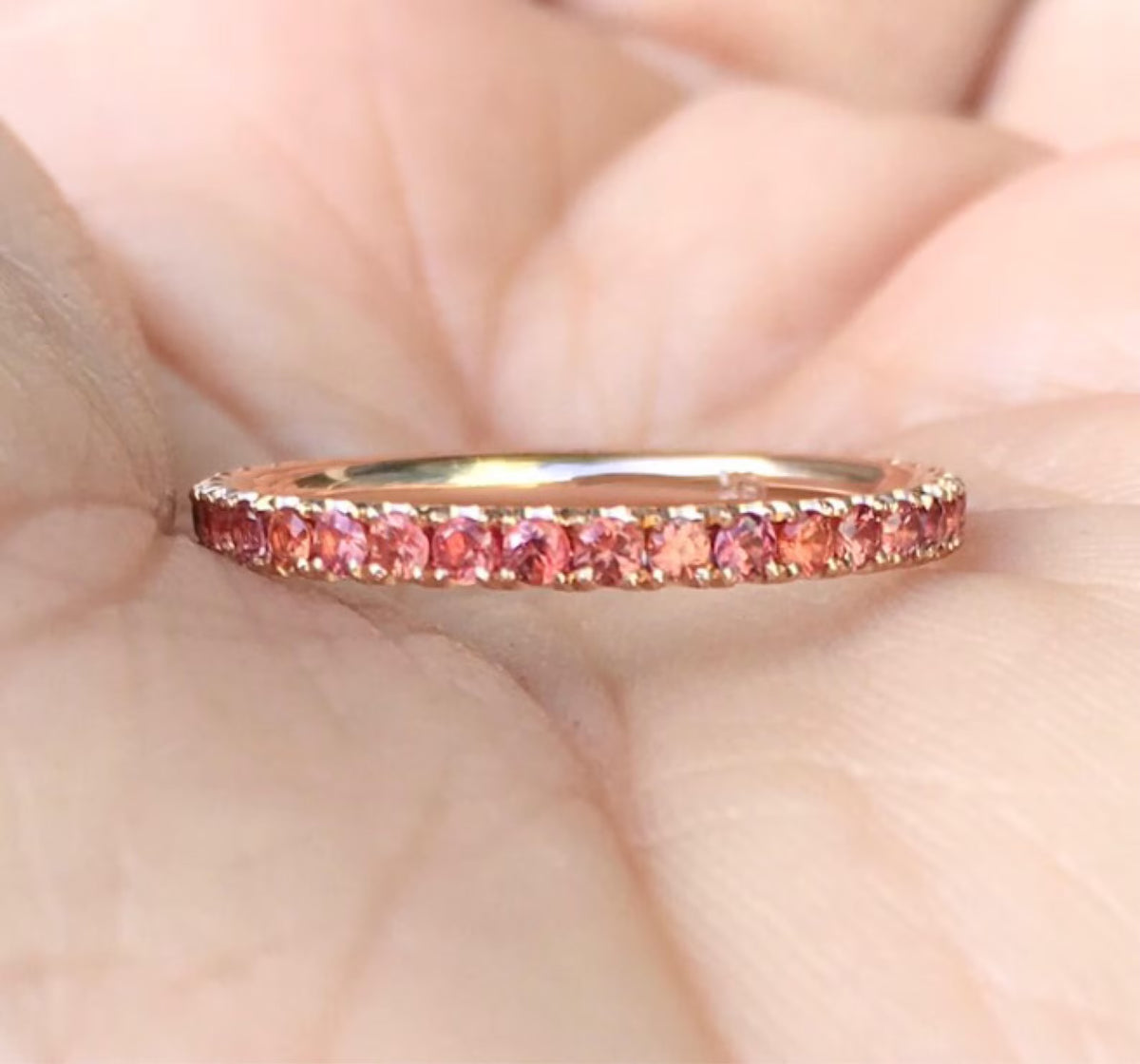 A rose gold eternity ring with a row of round pink gemstones, shown resting on a person's palm.