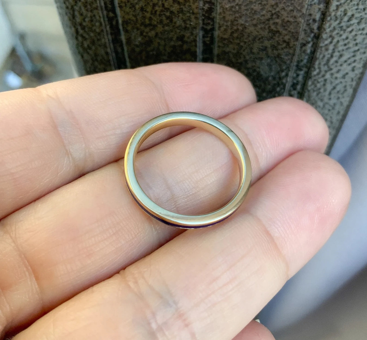 A minimalist, polished two-tone metal band ring resting on a person's fingers. The ring features a gold outer band and a silver inner band, shown close-up against a blurred background.
