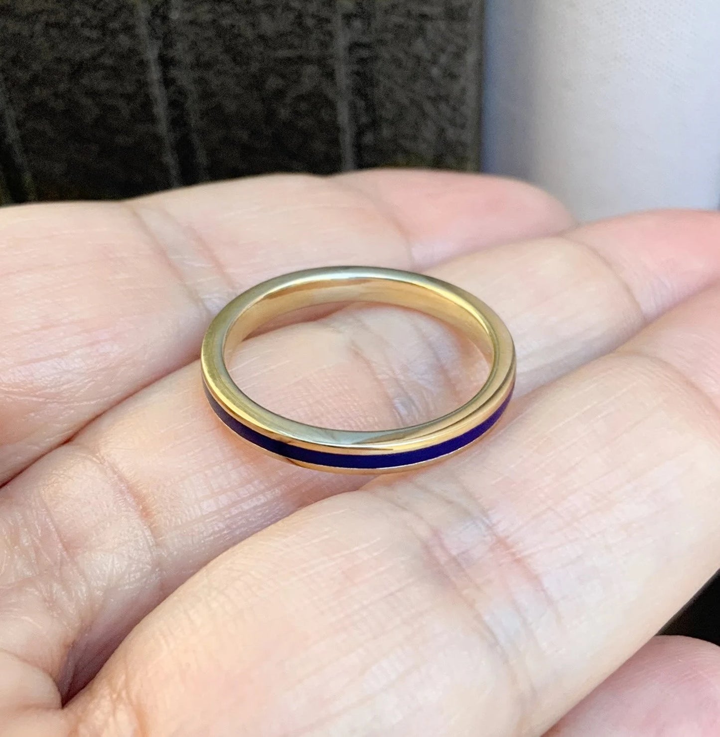 A gold band ring with a thin dark blue enamel stripe, resting on an open hand.