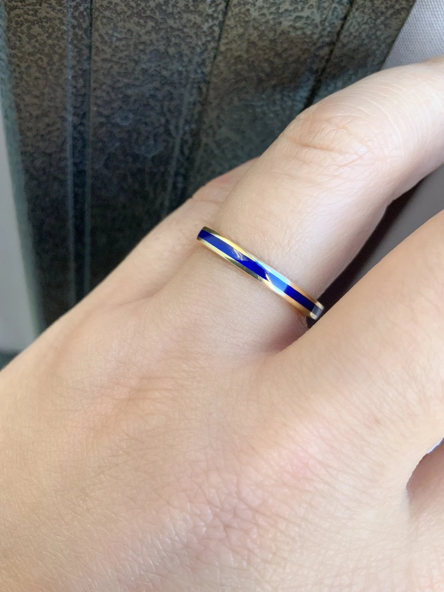 A close-up of a hand wearing a slim ring with a gold band and a central inlay of blue and white marbled material.