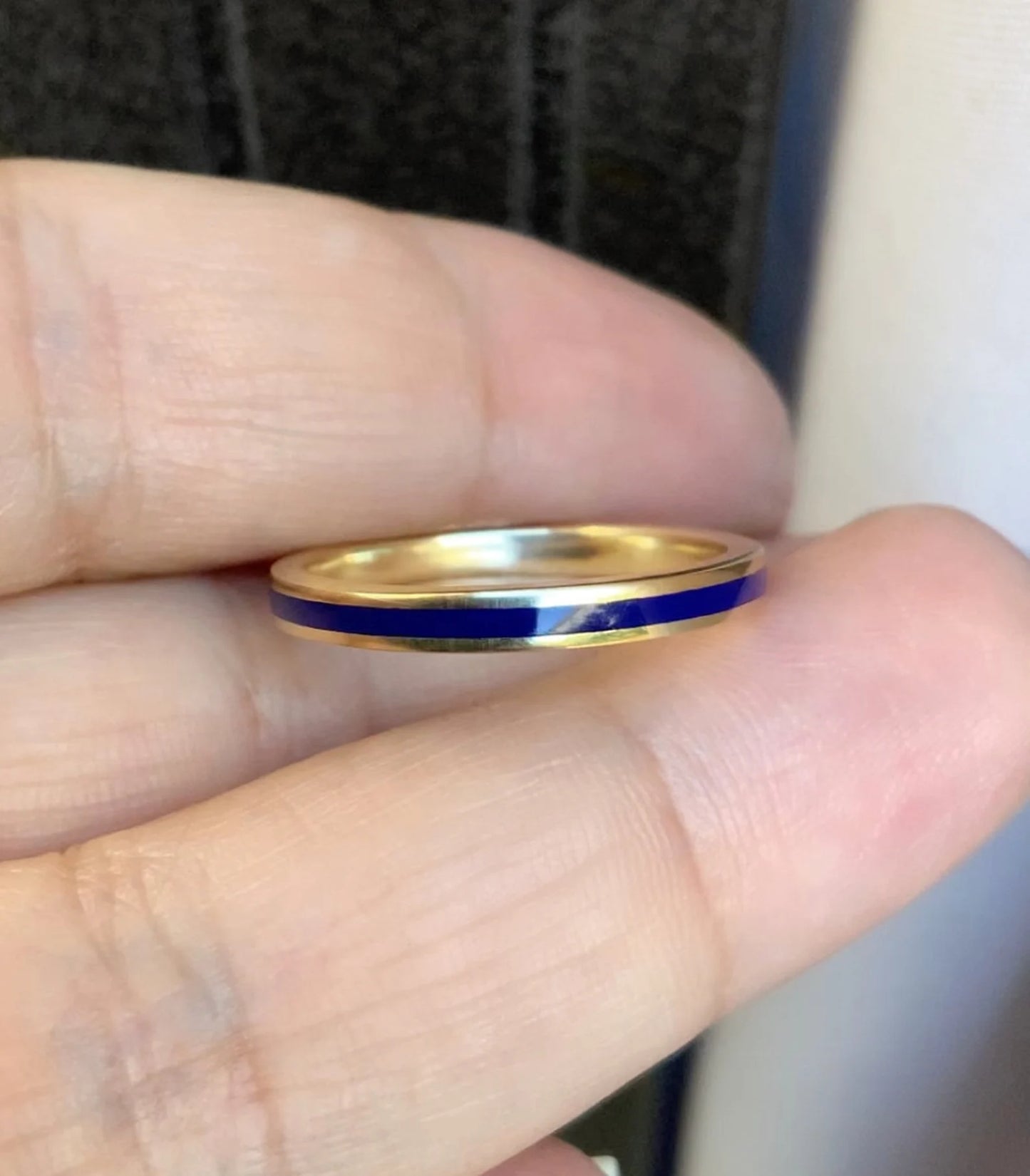A thin gold band ring with a vibrant blue inlay, held between a person's fingers.