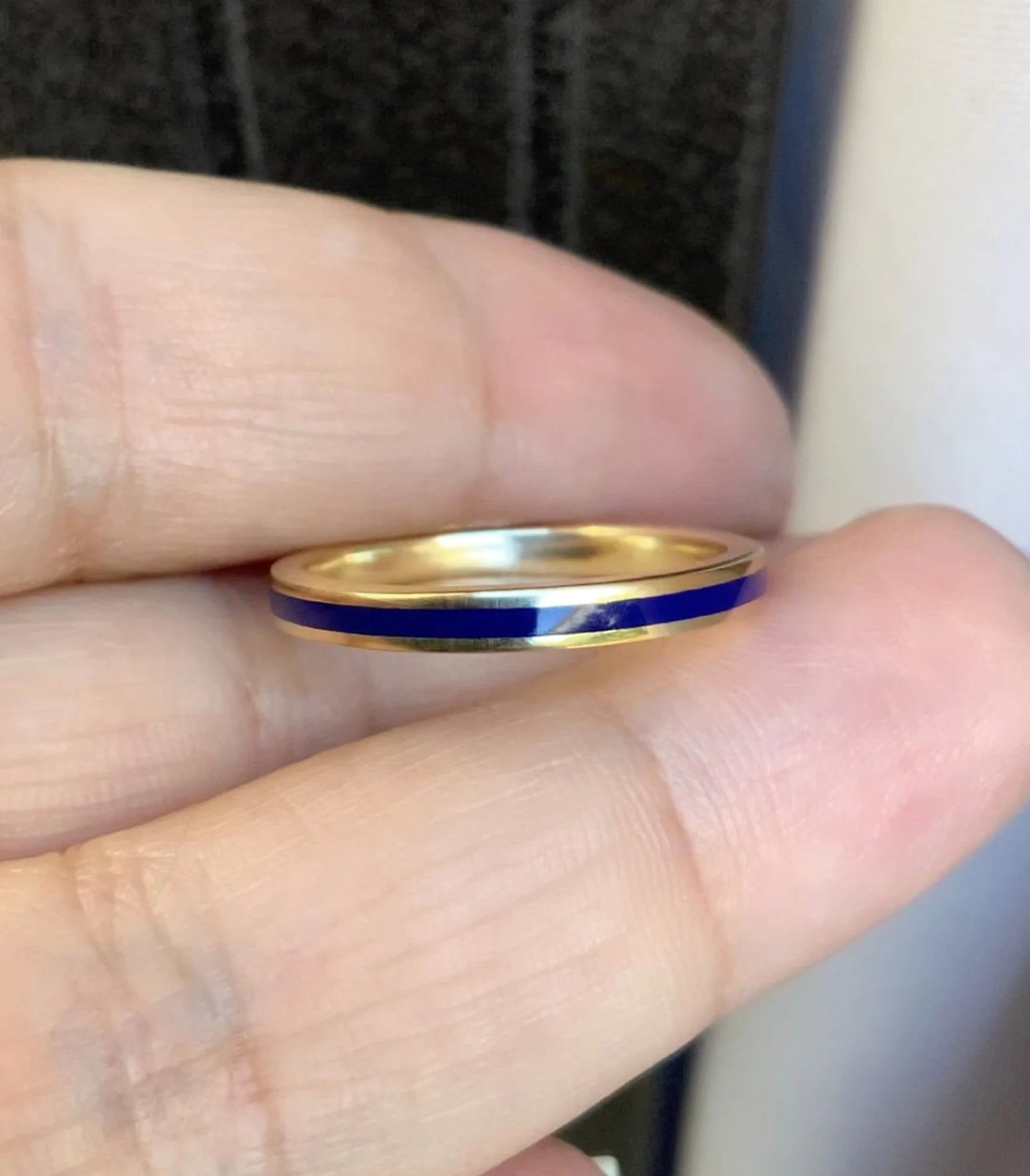 A thin gold band ring with a vibrant blue inlay, held between a person's fingers.
