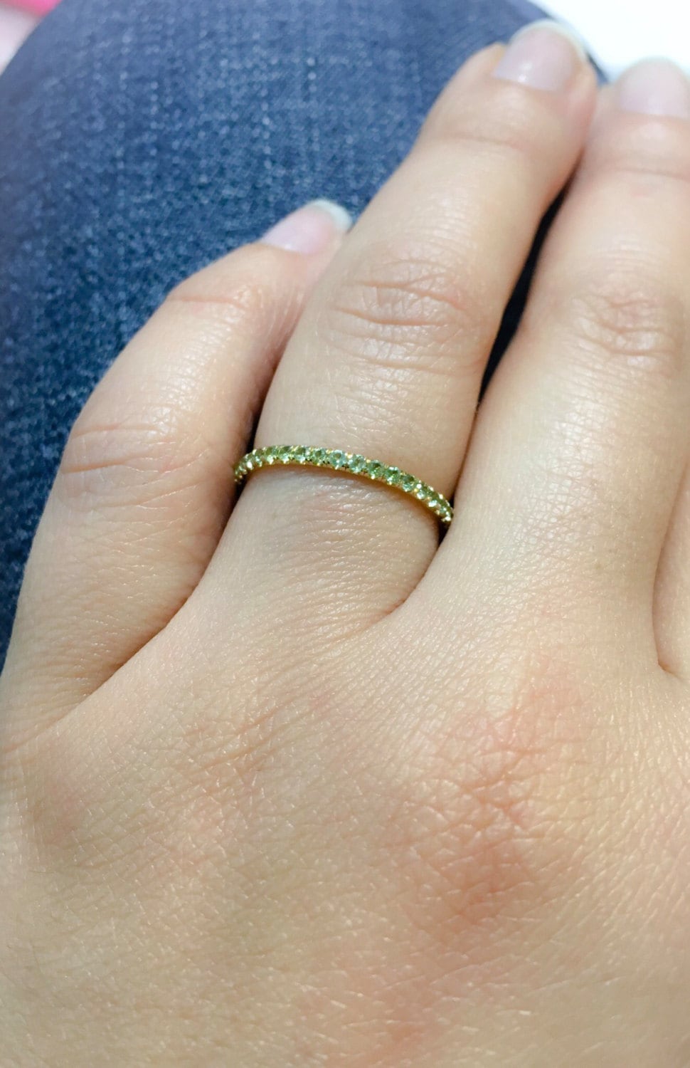 Natural peridot pavé stacking ring in yellow gold on finger, slim 1.8mm eternity band profile against denim background