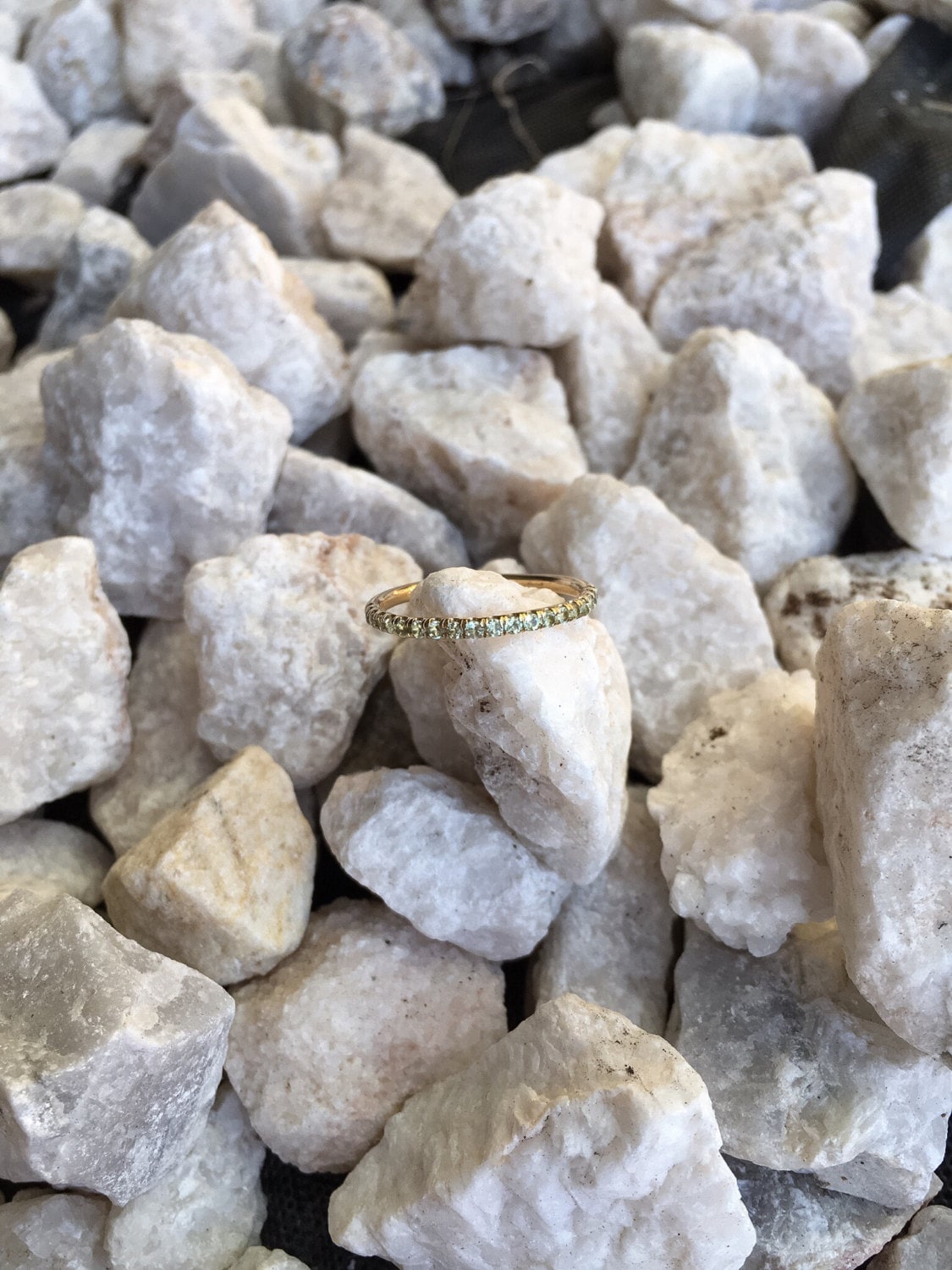 Natural peridot pavé wedding band in yellow gold resting on white stones, outdoor light showing green gemstones and warm gold setting
