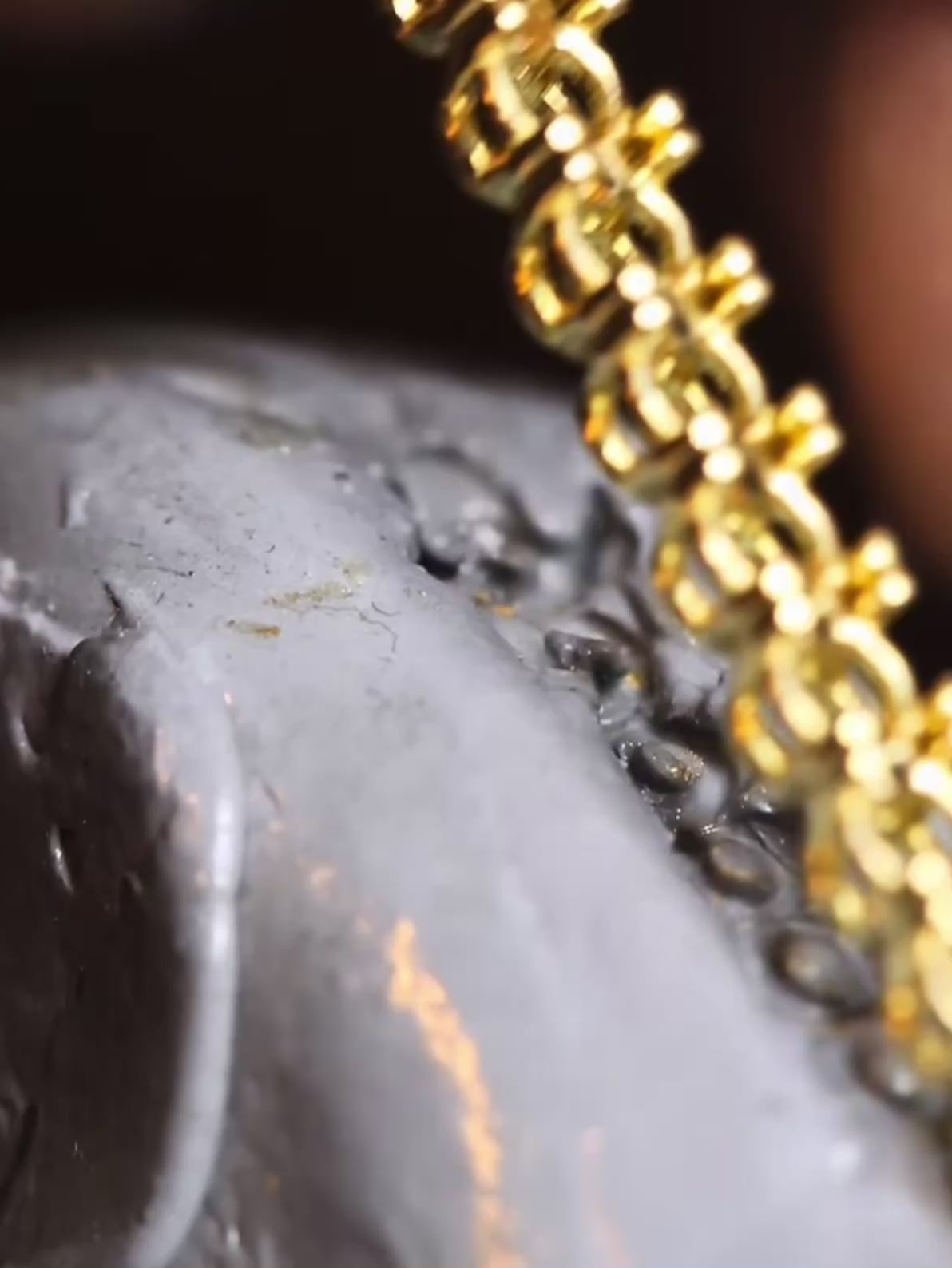 Load video: man's hands creating a gold tennis bracelet, setting diamonds into prongs, polishing the bracelet